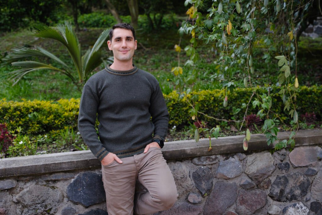 Simon Erlich leaning against a textured rock wall with a green vine, conveying a calm and grounded presence.